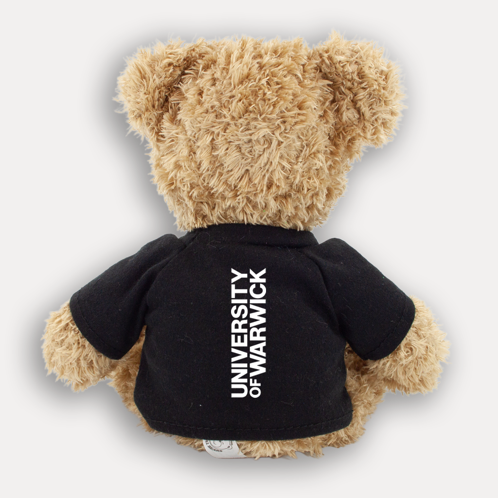 A small, light brown teddy bear from the back wearing a black t-shirt with a white University of Warwick logo running down the middle, shown on a light grey background. 