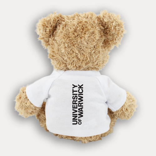 A plush teddy bear from the back with light brown fur wearing a white short-sleeve T-shirt with a black University of Warwick logographic running up the middle, shown against a light gray background.