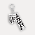 A University of Warwick keychain featuring a silver metal split ring and chain, with a shield-shaped crest charm and a diagonal ribbon charm printed with the text 'UNIVERSITY OF WARWICK' in black and white, shown on a light grey background.